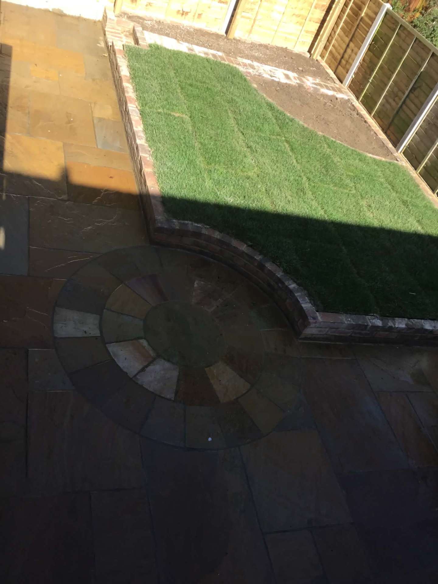 Slate paving with circular feature and raised lawn