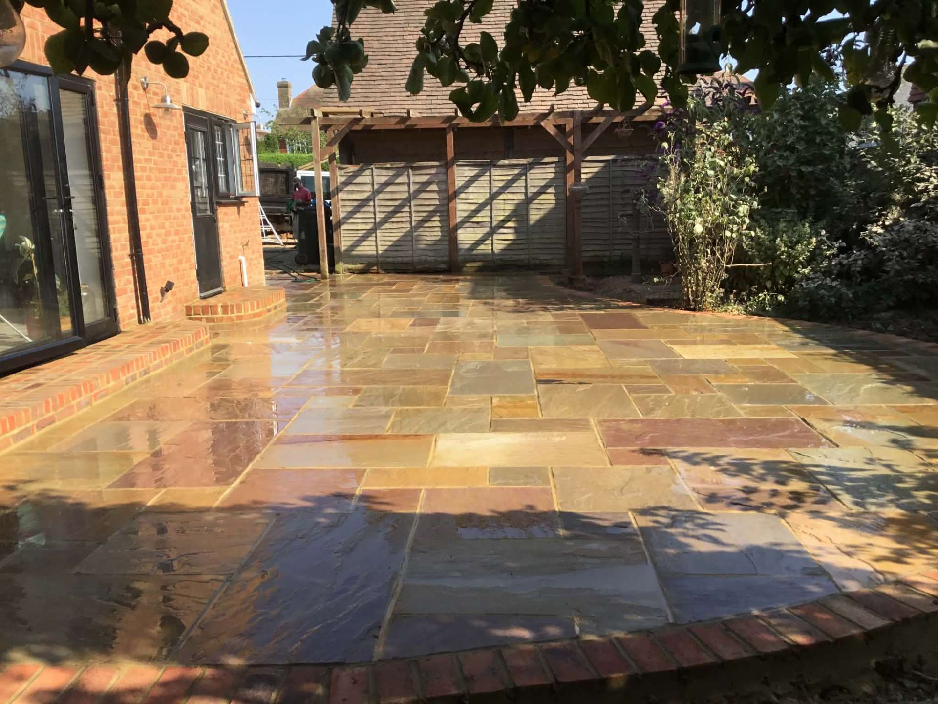 Indian sandstone patio with brick edging beside brick house