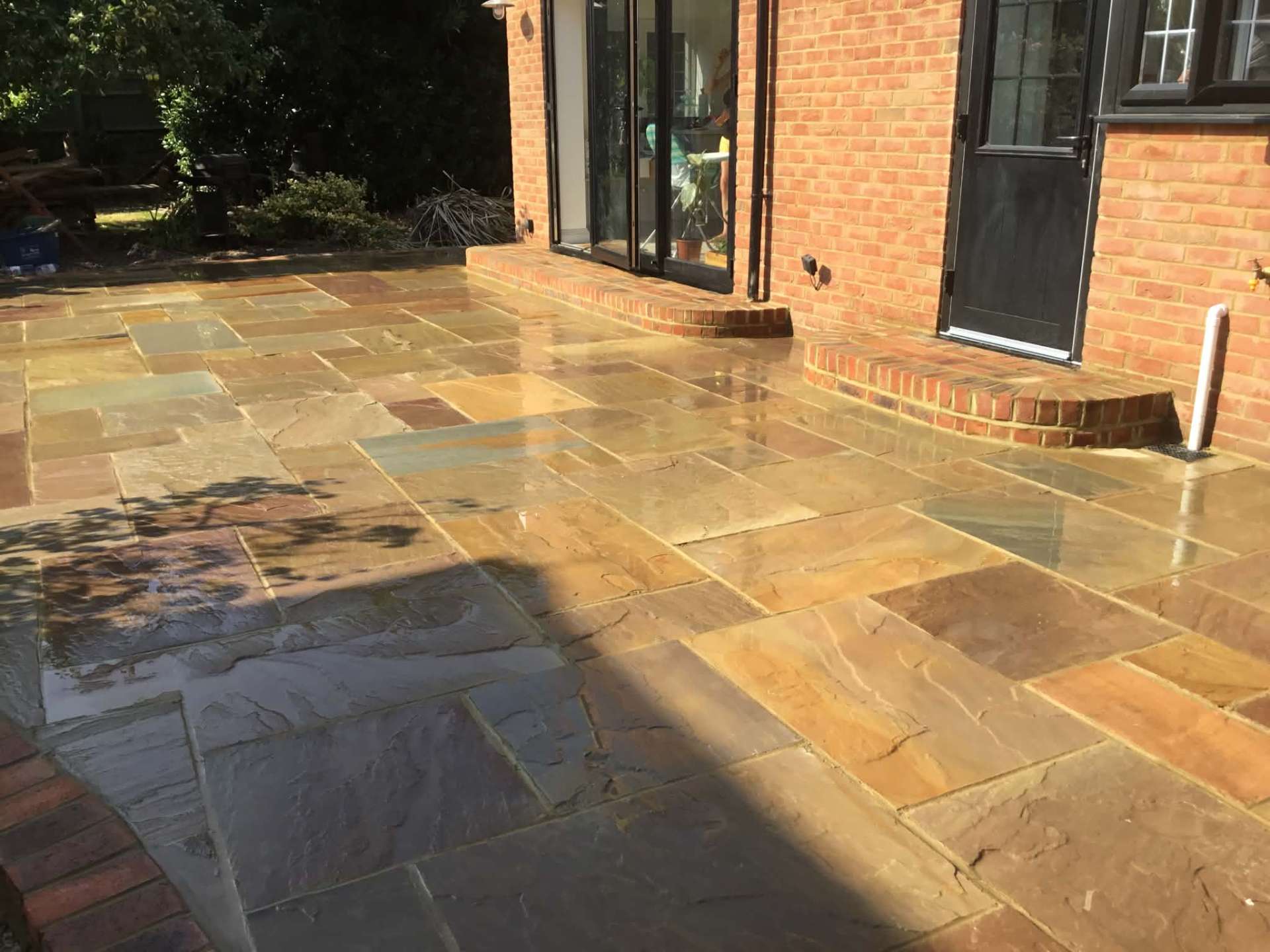 Indian sandstone patio with curved brick step beside bifold doors