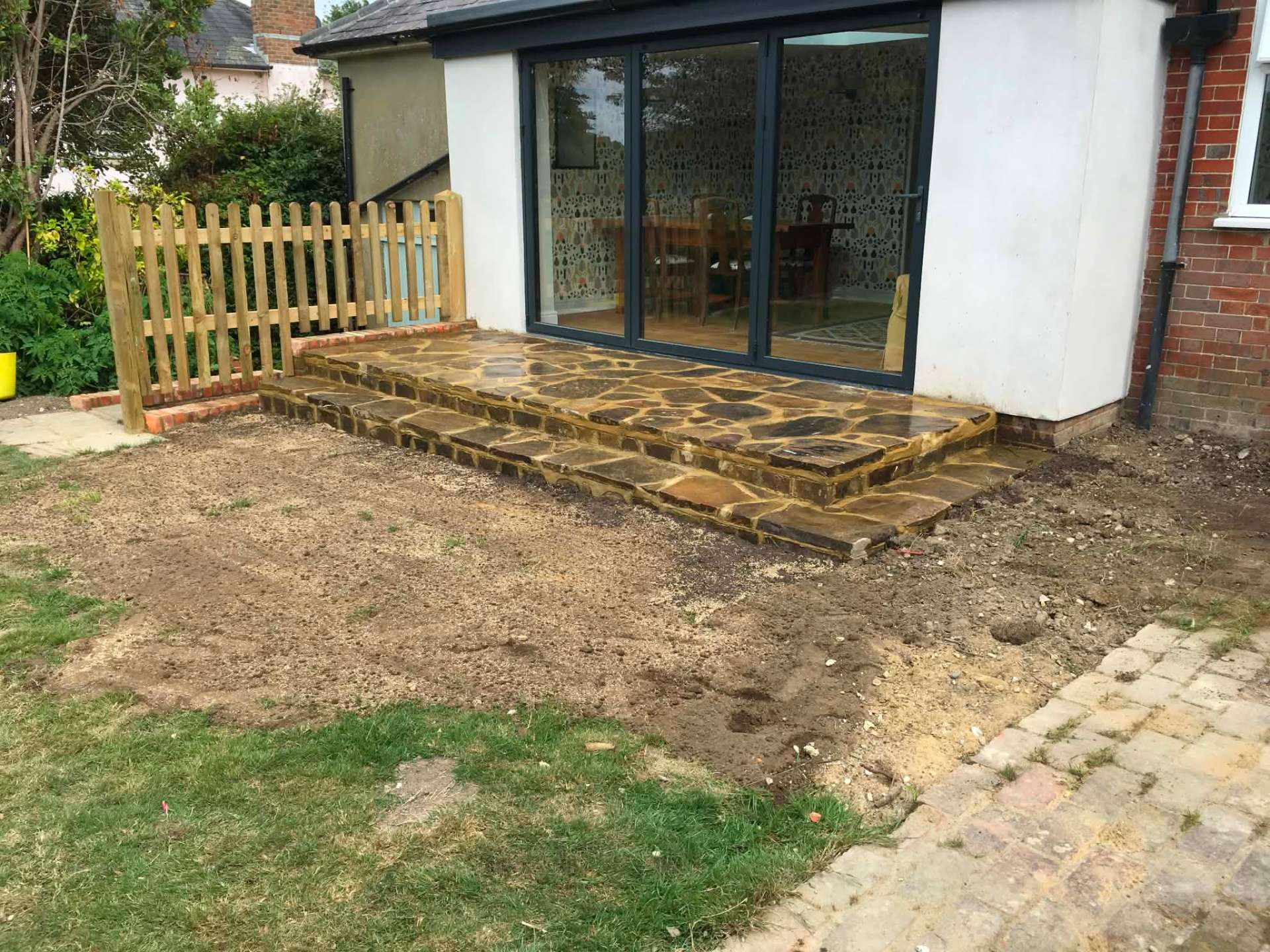 Crazy-paving steps from bifold doors with picket gate