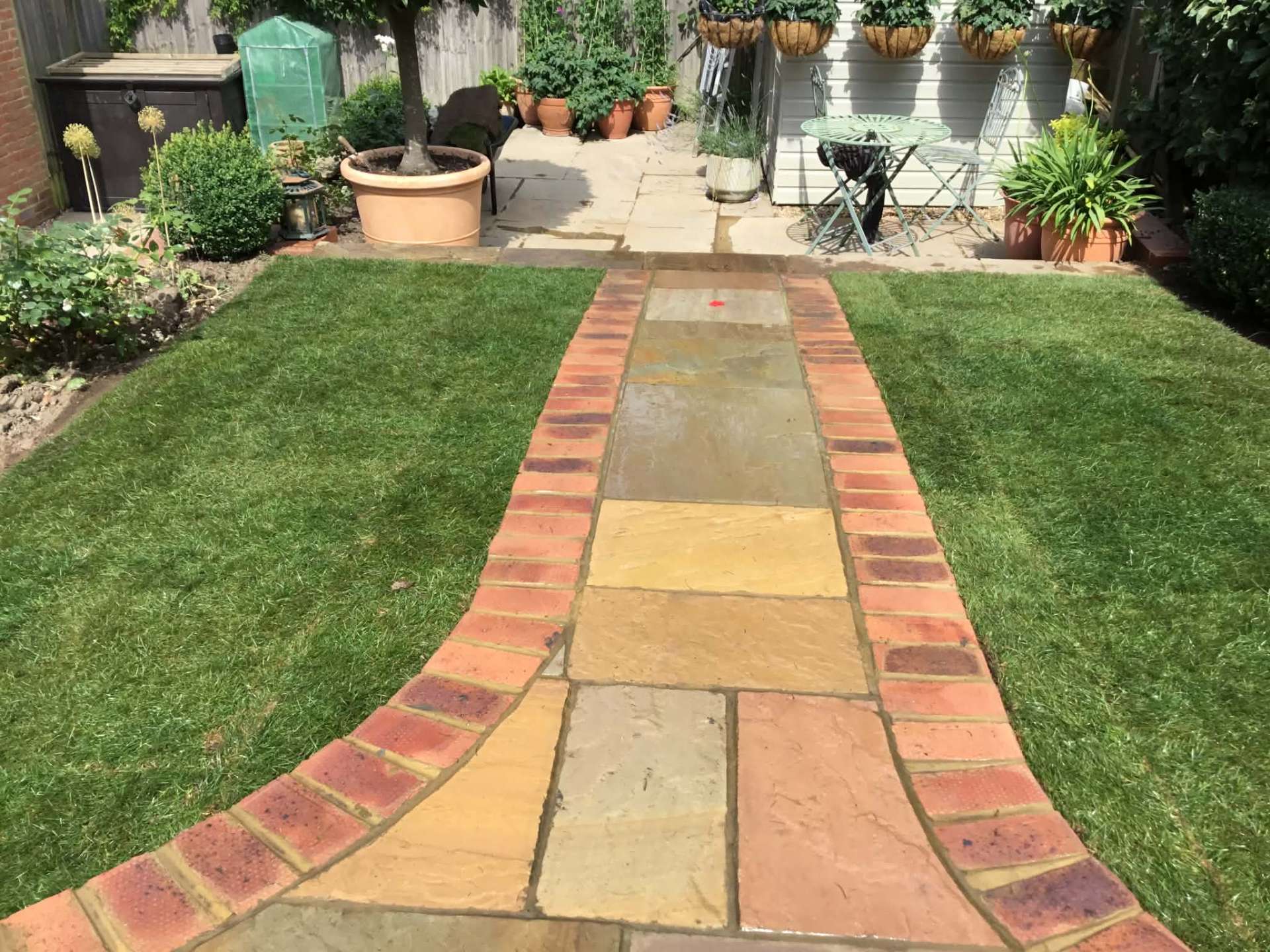 Sandstone path with brick edging cutting through fresh lawn