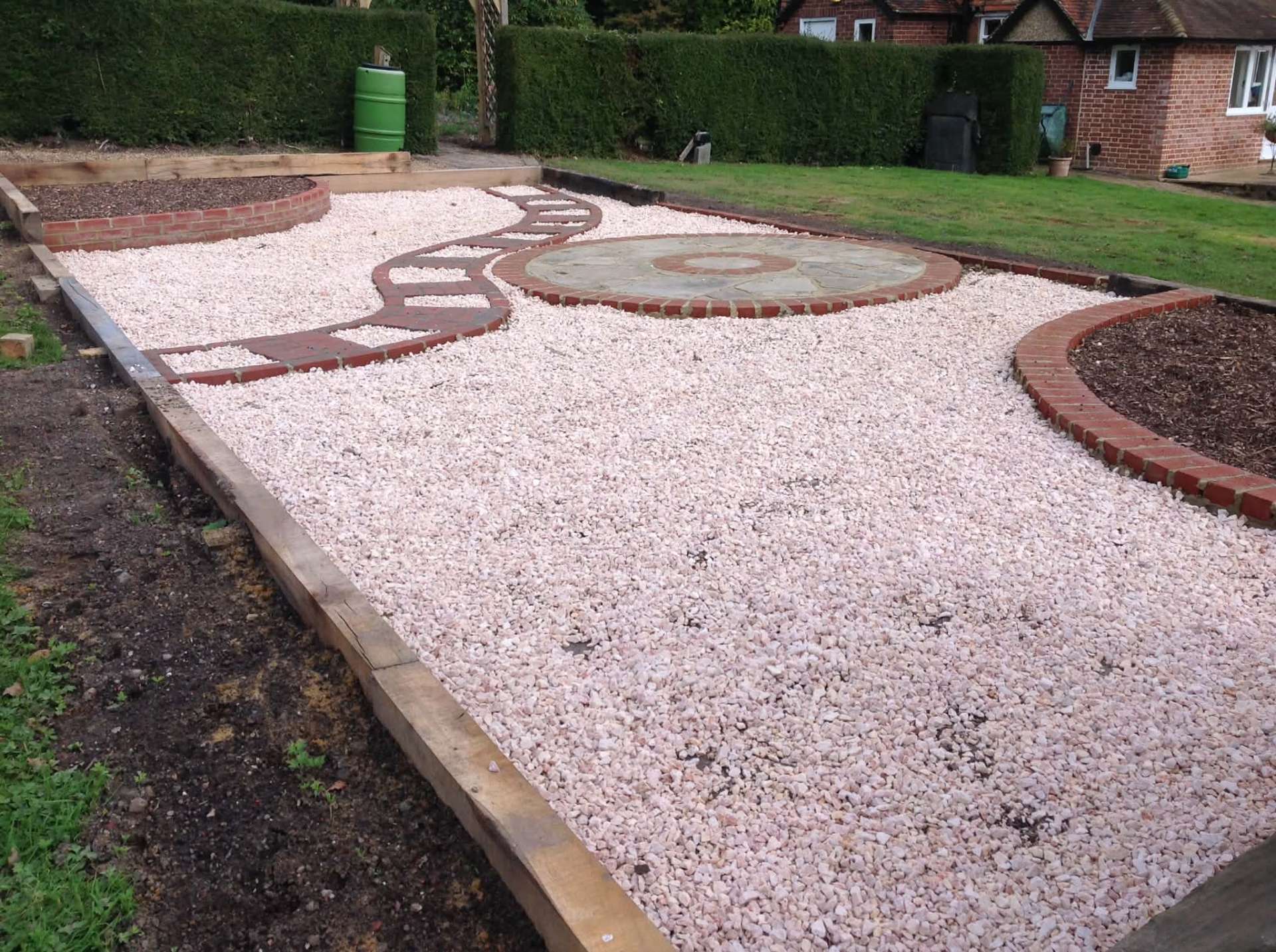 White gravel garden with circular millstone and brick-edged beds