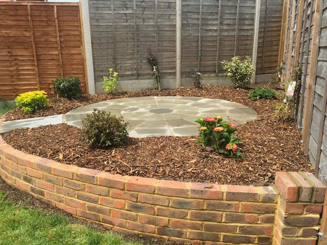 Circular sandstone patio set into curved brick-walled raised border