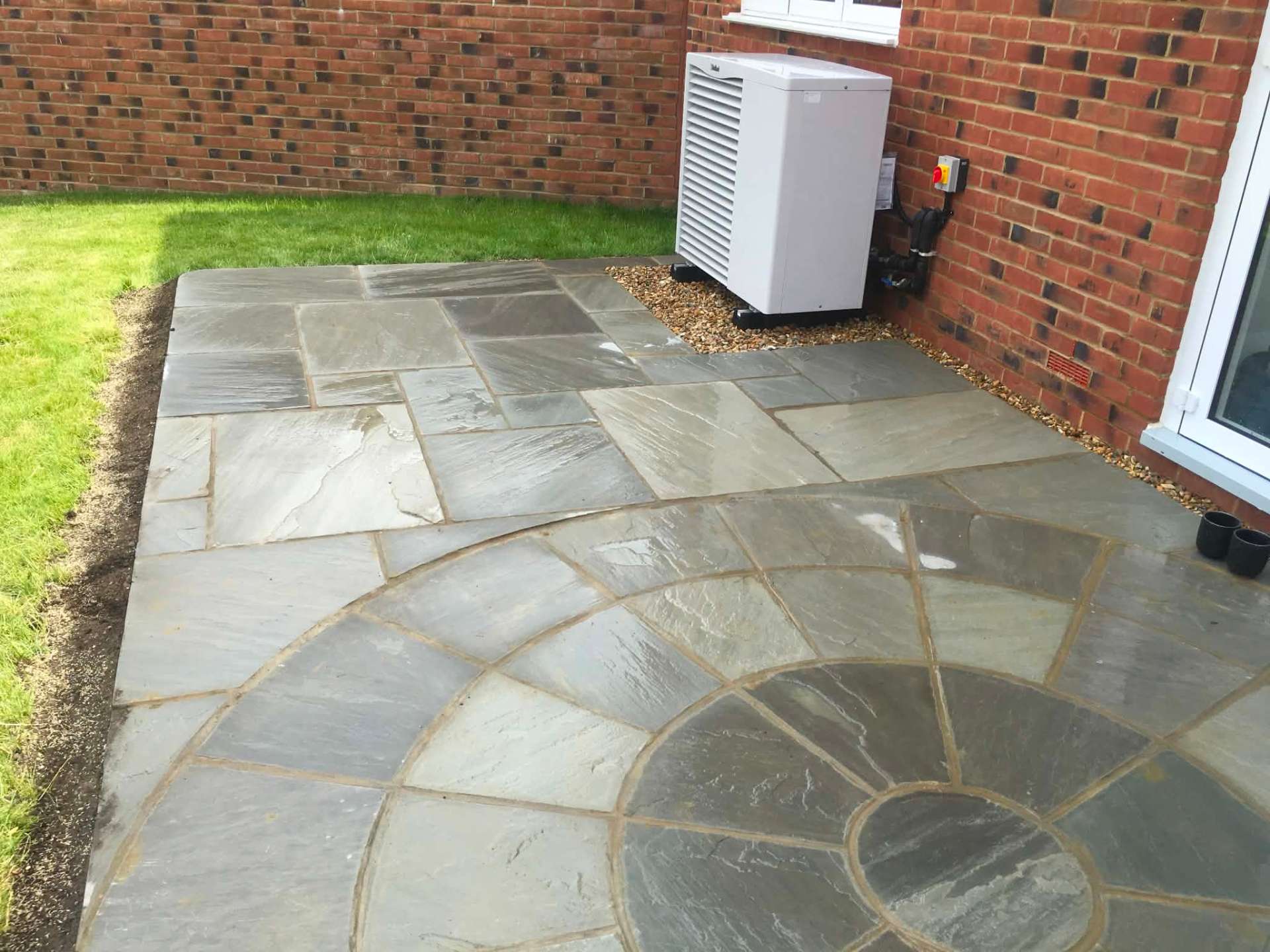 Indian sandstone patio with circular feature beside new-build home